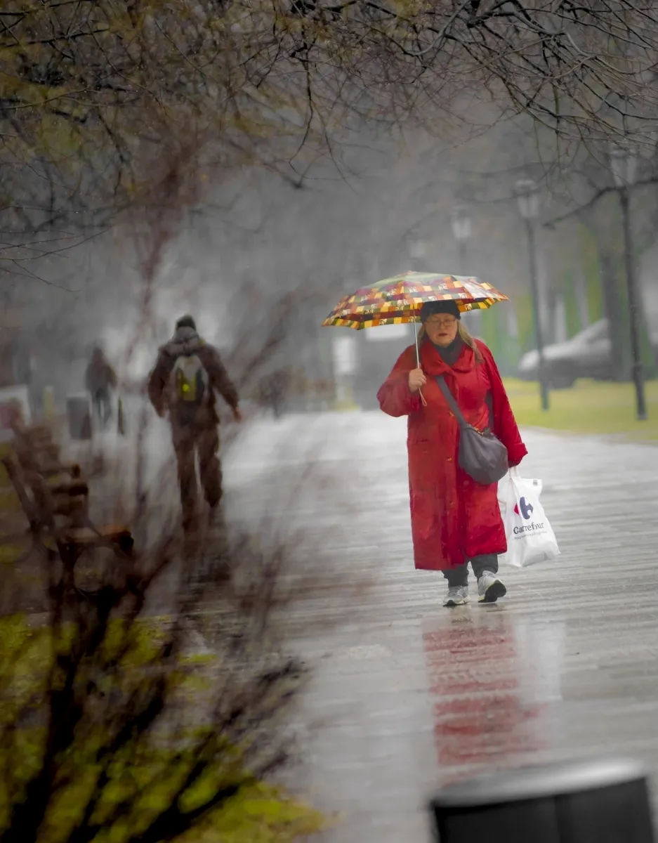 Woman in a red coat carrying a colorful umbrella in the rain